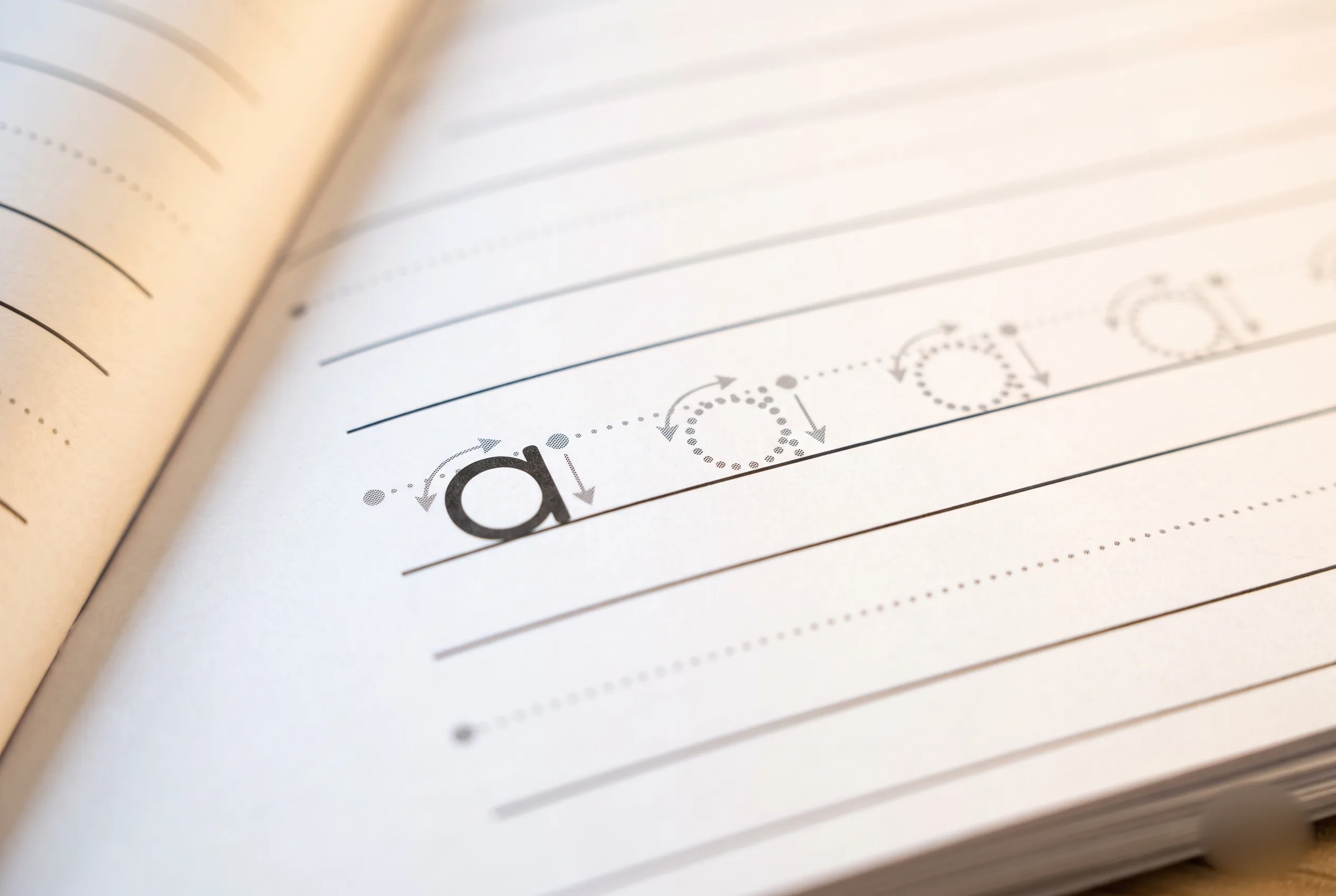Close-up of a handwriting practice page showing dotted midline guides and directional arrows for tracing the lowercase letter a